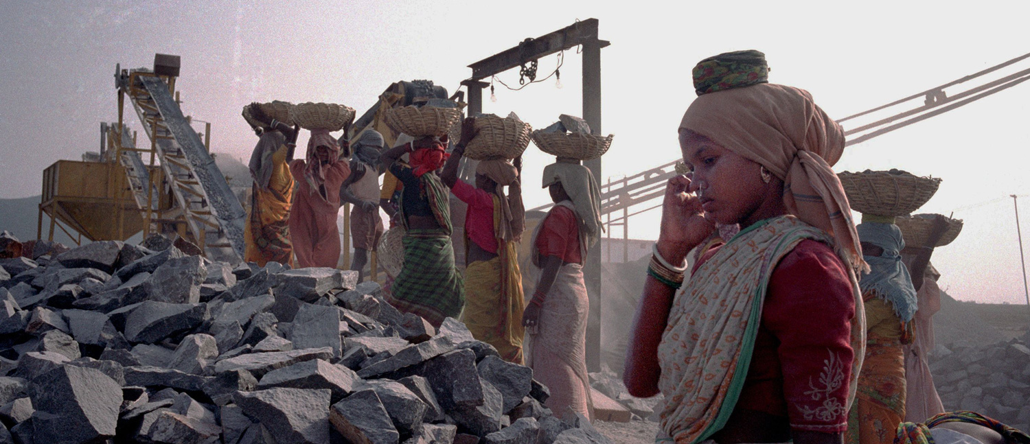 Girl takes a break from carrying rocks at a gravel quarry.