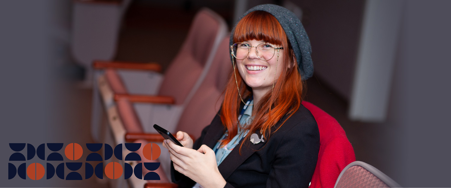 Female student with red hair and round glasses smiles at the camera. 