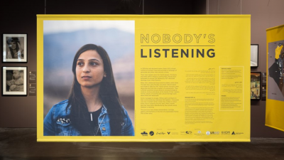 A photo of a section of the exhibit with a yellow banner that has a photo of a women on the left. The woman has long black hair and looks to the right away from the camera. On the left is small text with a header that reads "Nobody's Listening."